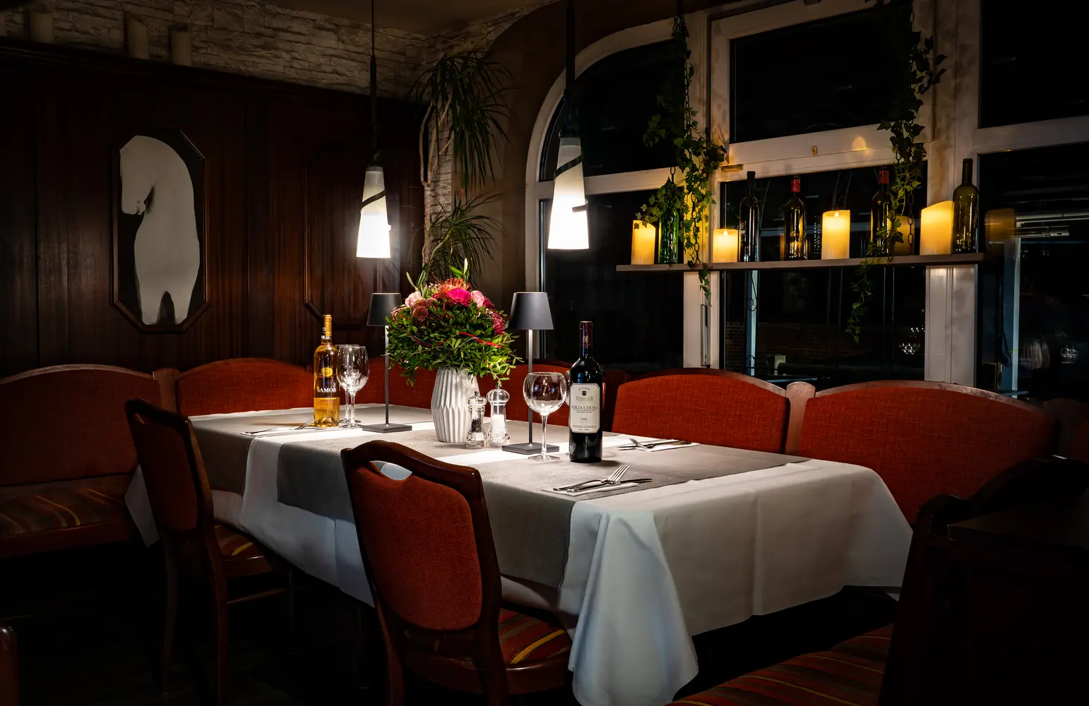 Ein festlich gedeckter Tisch mit Kerzen, Blumen, Wein und warmem Licht im Restaurant