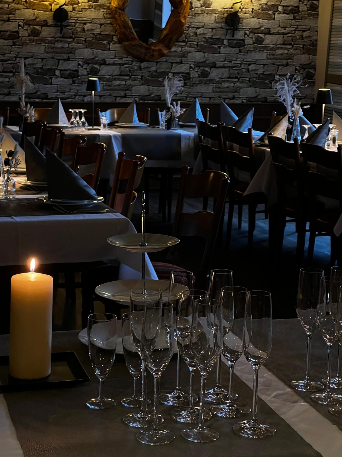 Ein elegant gedeckter Tisch mit Kerze und mehreren leeren Sektgläsern im dunklen Restaurant